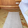 Solid handwoven wool runner rug at the foot of a wooden bed, placed on natural pine flooring.