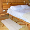 Undyed wool runner rug beside a wooden bed, placed on light pine flooring.