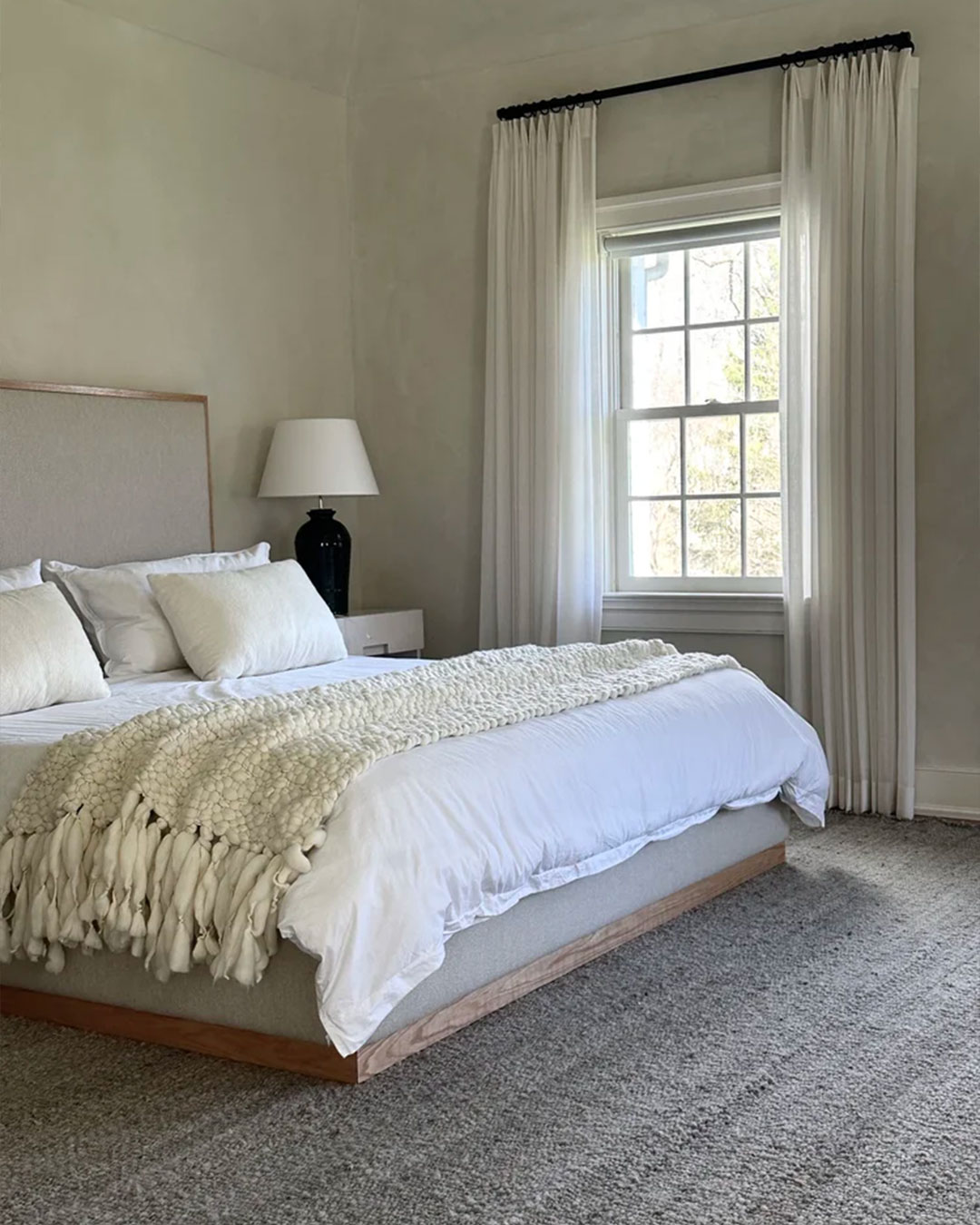 Solid gray wool rug in Smokey Gray at the foot of a bed in a light-filled bedroom