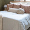 Beige and Natural White round cushion with radial pattern, placed on a made bed.