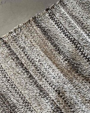 Diagonal view of the Pepper speckled wool rug laid across a concrete floor