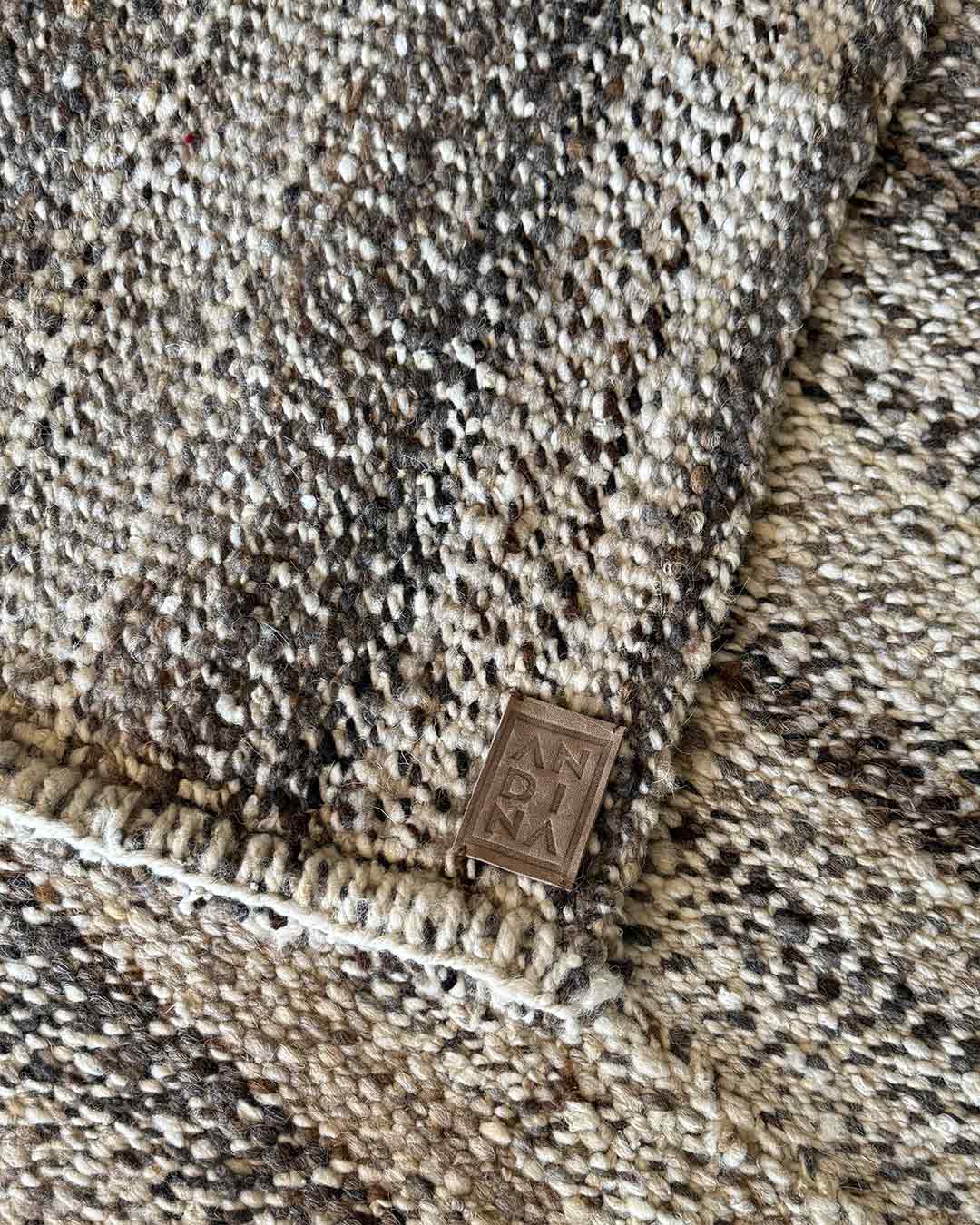 Detalle macro de la alfombra Lisa Pimienta con la etiqueta de cuero ANDINA en la esquina doblada