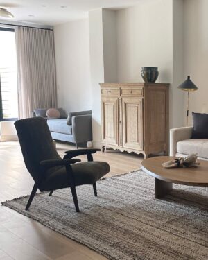 Speckled wool area rug in Pepper styled in a living room with a dark green armchair and wooden cabinet