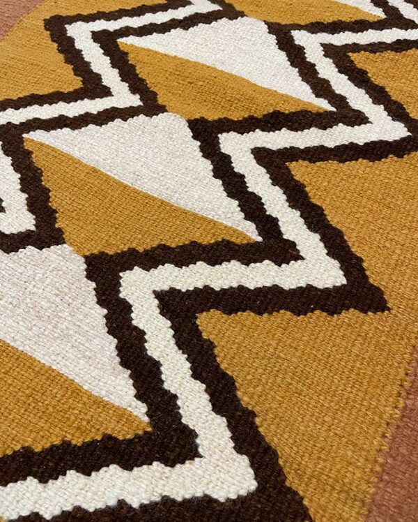 Close-up detail of a handwoven Qom textile with a traditional geometric design featuring different shapes and colors.