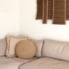 Natural White square cushion with pom poms and Beige round cushion without pom poms on a light sofa.
