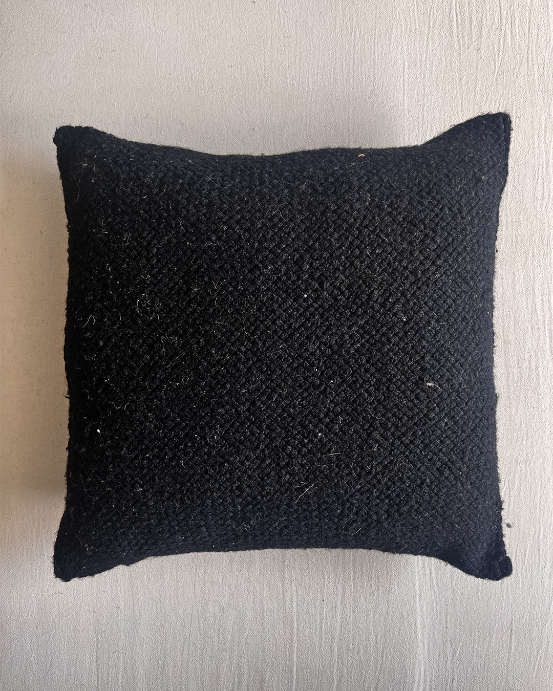 Almohadón cuadrado de lana color negro, visto desde el frente.