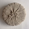 Back of a beige round cushion made of handwoven wool, with visible woolen tie closure.