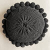 Black-colored round cushion with handmade pom poms, shown from the back.