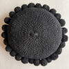 Black-colored round cushion with handmade pom poms, shown from the front.