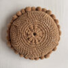 Back of a camel-colored round wool cushion with visible woolen cords.
