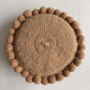 Camel-colored round cushion with handmade pom poms, shown from the front.
