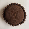Chocolate brown-colored round cushion with handmade pom poms, shown from the front.