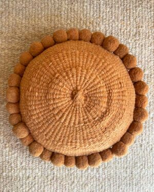 Camel pom pom cushion on a natural white plain rug by Andina Decor.
