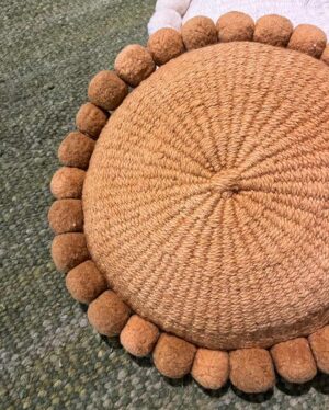 Camel pom pom cushion on top of a Yerba wool rug by Andina Decor.