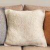 Three square wool cushions in Gray, Natural White, and Camel placed on a beige sofa.