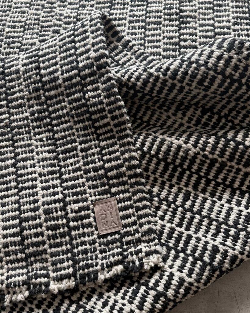 Folded corner of the Comb wool area rug with the ANDINA leather label
