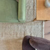 ala de estar con alfombra de lana a rayas en tonos beige (arena) y blanco (natural), debajo de sillones verdes y marrones de terciopelo.
