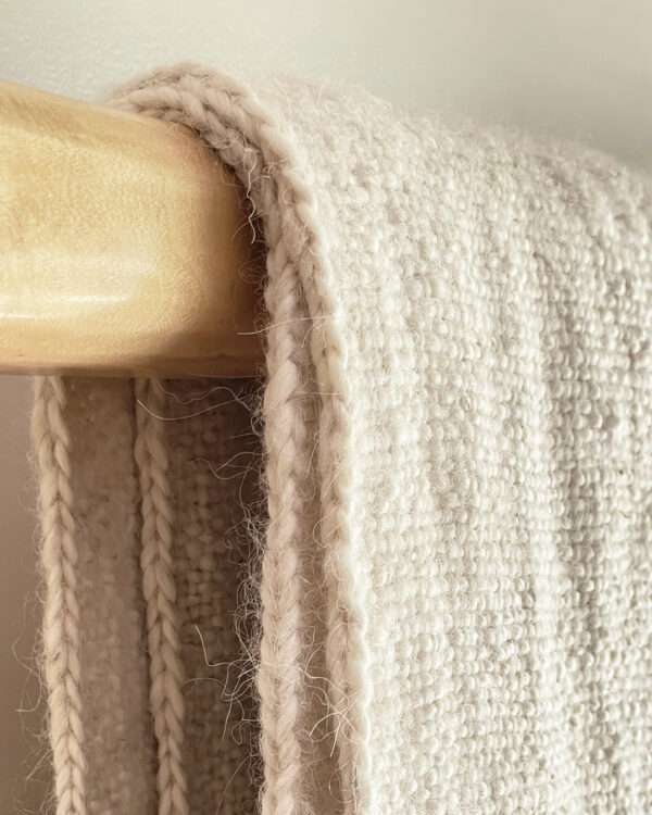 Natural llama fibre throw blanket with fringes on a wooden bench.