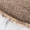 Close-up of the hand-stitched edge of a round brown rug on a concrete surface.