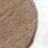 Round wool rug in wood tone (brown), partial top view on light concrete floor.