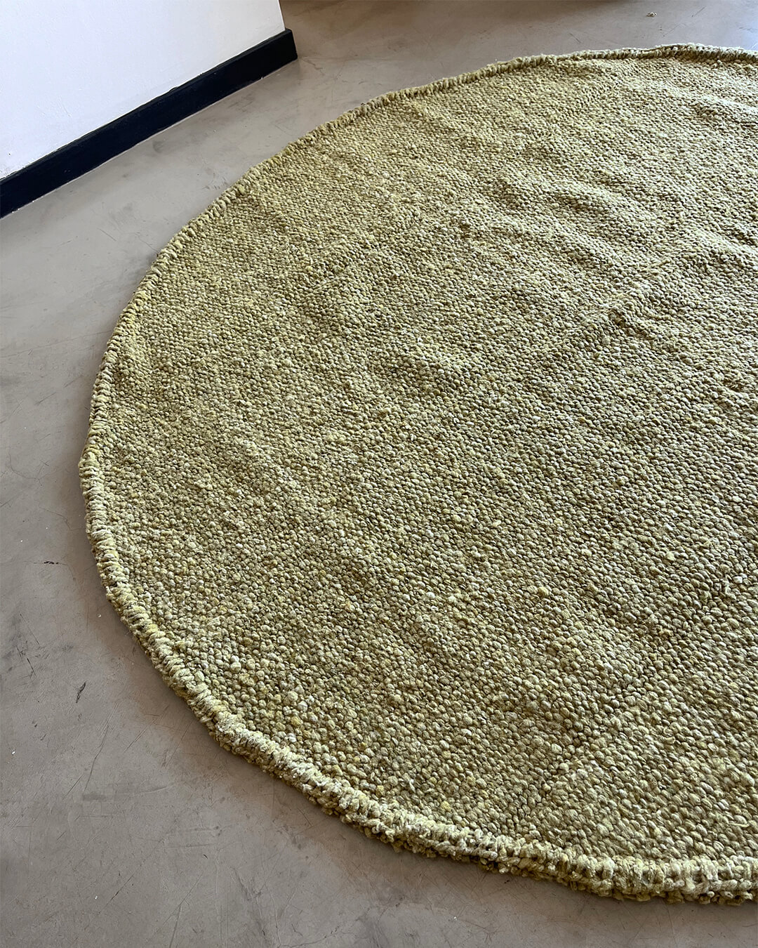 Yerba green round rug placed on a concrete floor with soft light from the side.