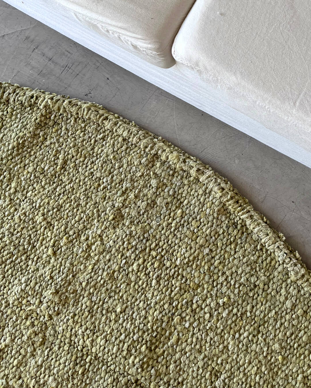 Close-up of the Round Rug in yerba green, placed beside a white bench with cushions.
