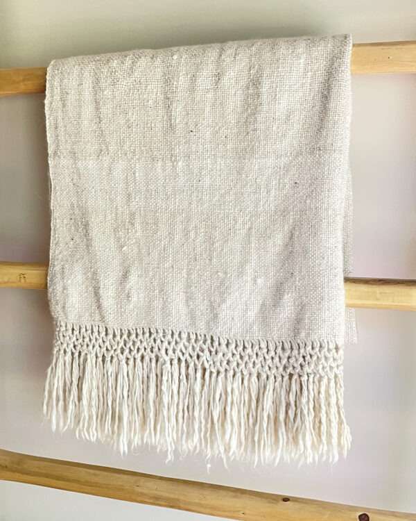 Natural llama fibre throw blanket with fringes on a wooden bench.