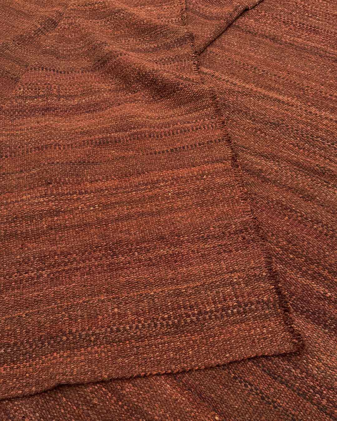 Folded edge of the solid burgundy wool rug showing the hand-finished border
