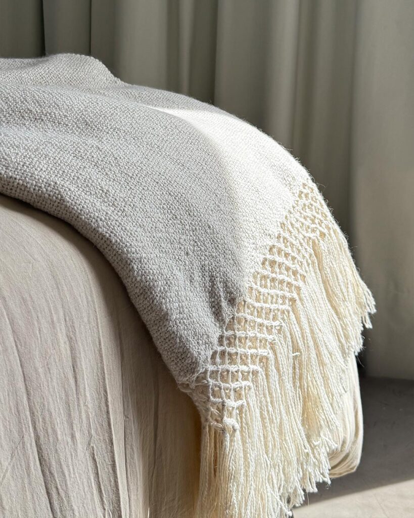 Llama throw blanket natural white draped over a bed with soft fringe — handwoven in Argentine Andes