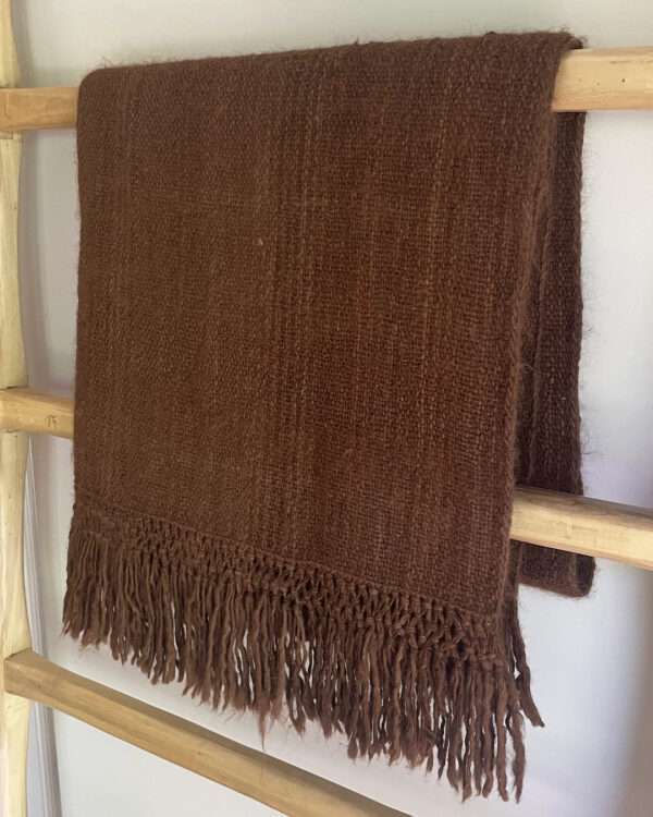 Brown frizzed llama throw blanket hanging on a ladder.