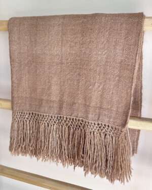 Beige llama fibre throw blanket with fringes on a wooden bench.