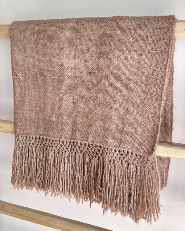 Llama Throw – Oat in undyed beige llama fiber, folded and displayed on a wooden rack.