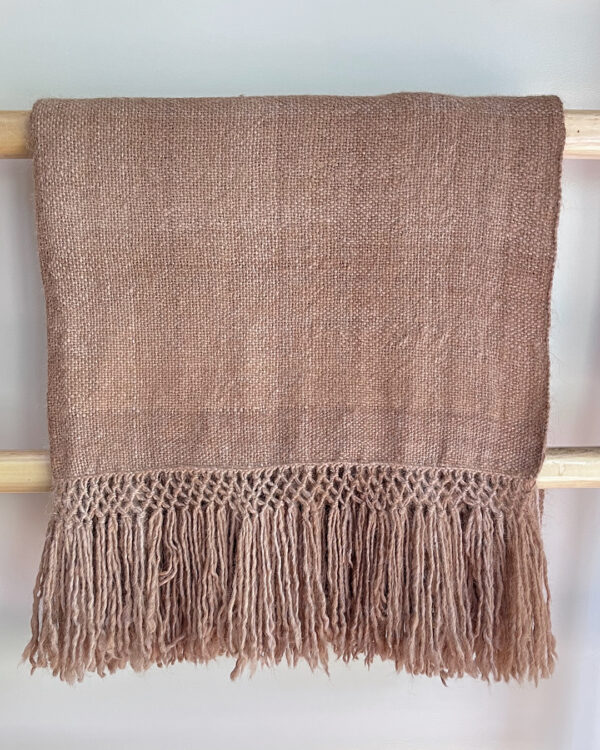 Llama Throw – Oat in undyed beige llama fiber, folded and displayed on a wooden rack.
