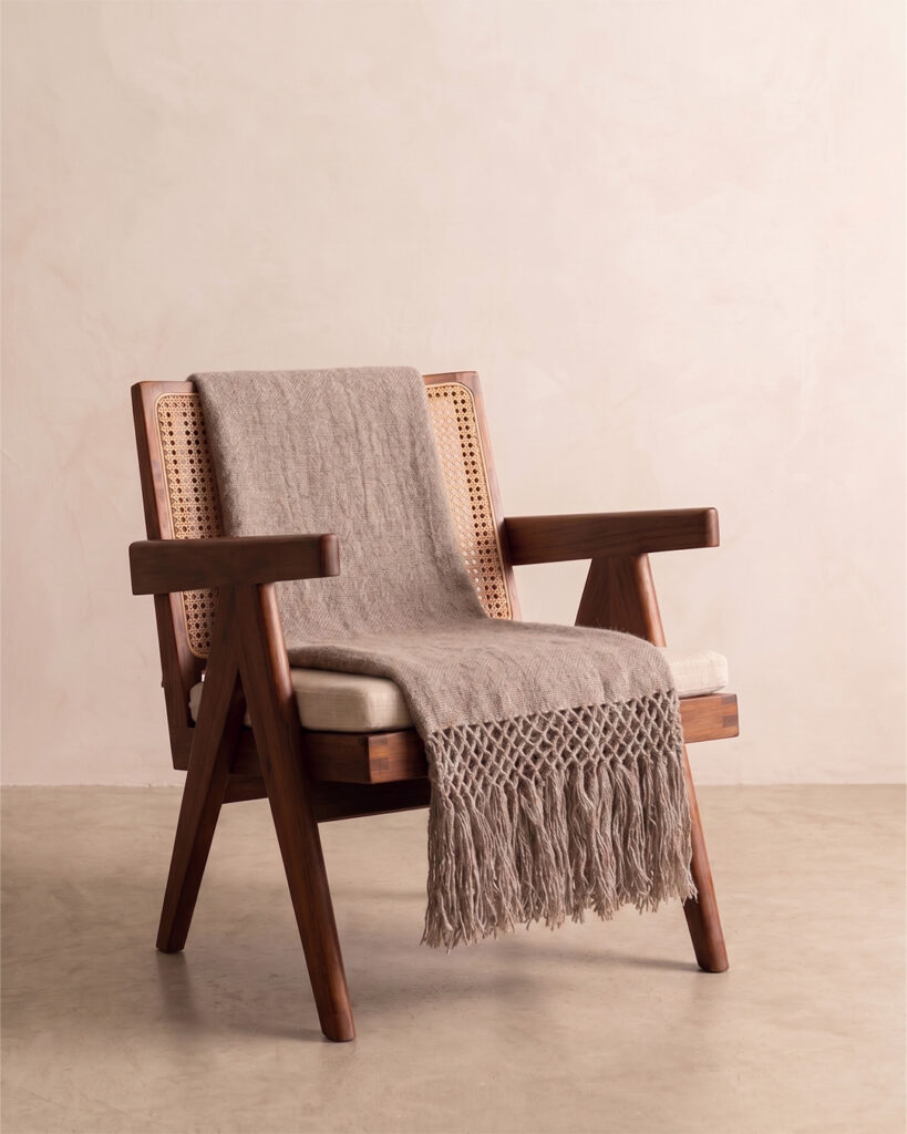Oat llama throw draped over a cane and wood armchair with knotted fringe