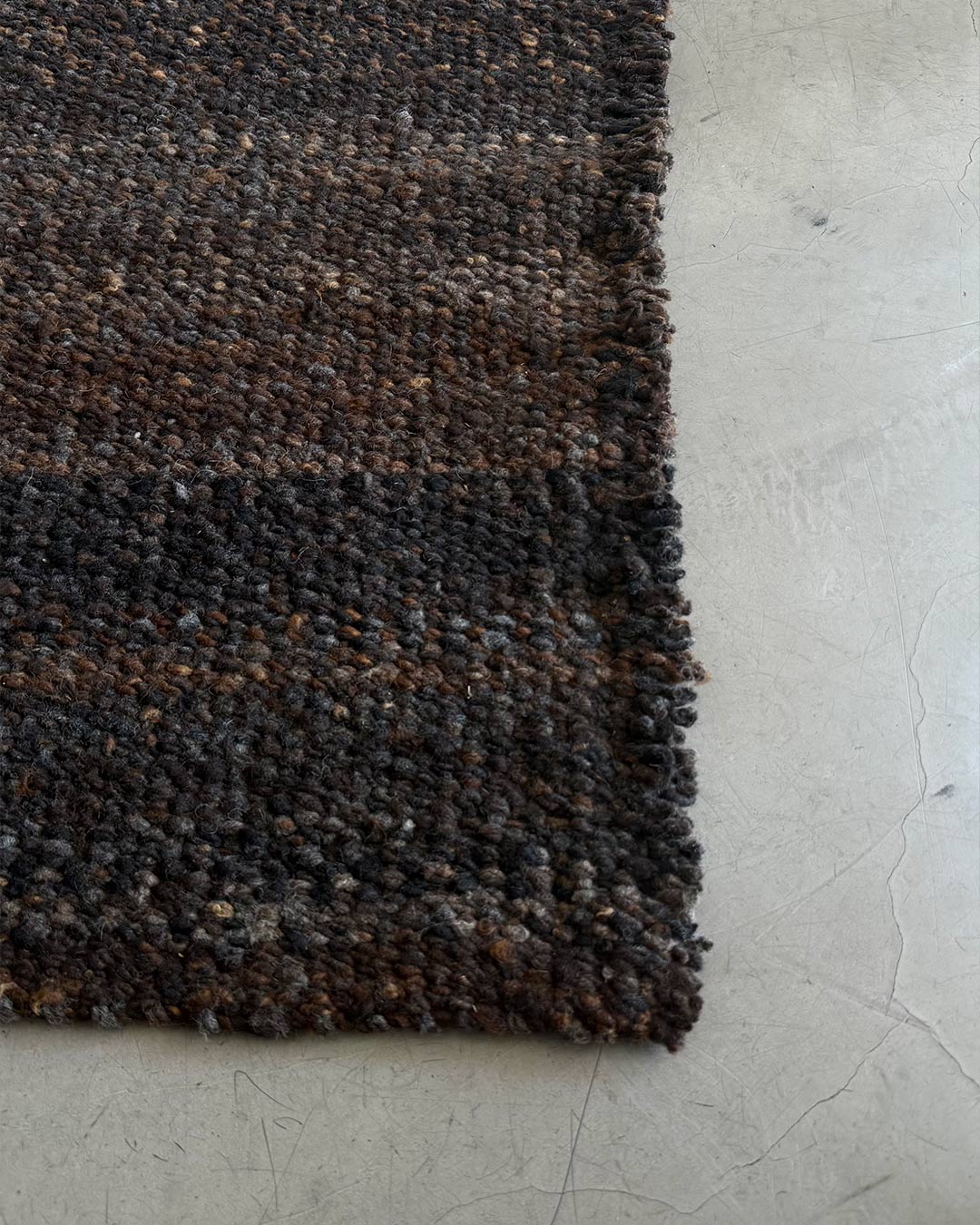 Straight corner detail of solid coffee wool rug on concrete floor