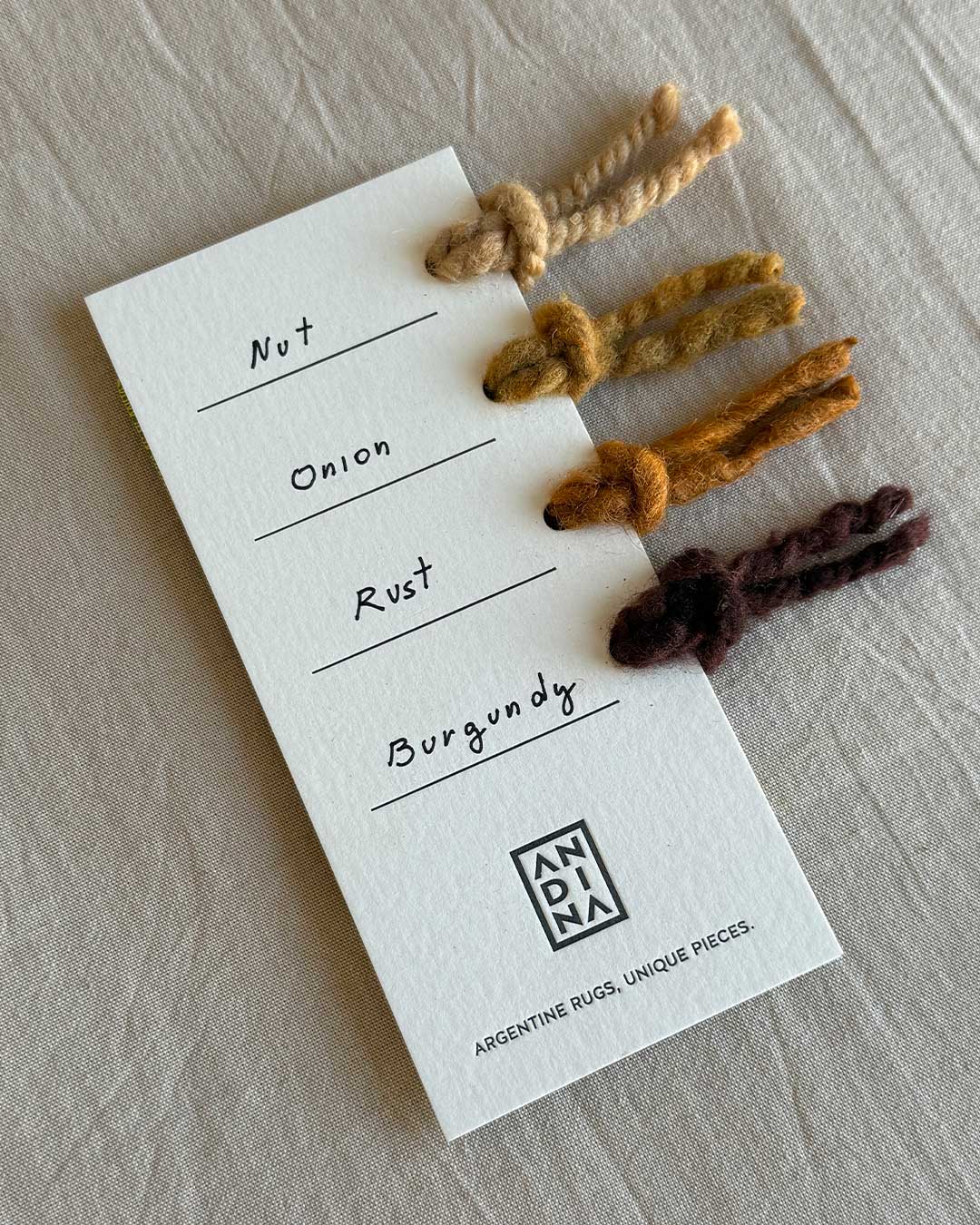 Yarn sample card with four natural wool colors by ANDINA: Nut, Onion, Rust, and Burgundy.