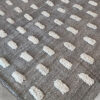 Alfombra tejida a mano en gris humo con detalles de pompones blancos.