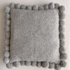 Gray-colored square cushion with handmade pom poms, shown from the front.