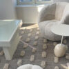 Alfombra gris con pompones blancos en un living moderno con sillones suaves y mesa auxiliar de mármol.