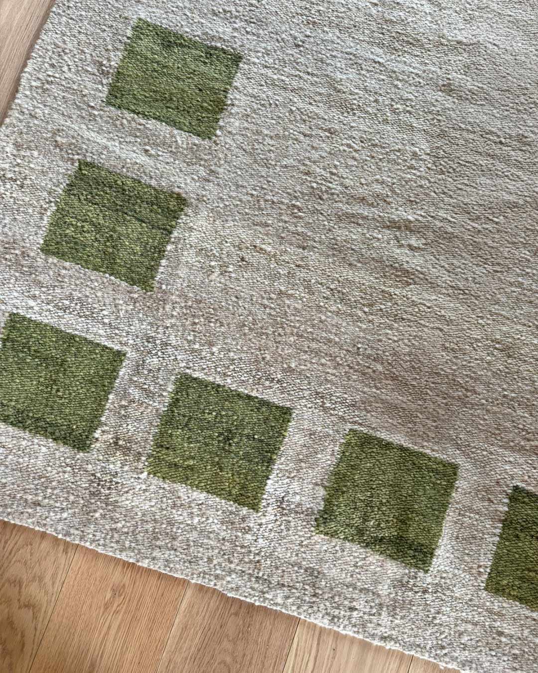Close-up of sand wool rug with moss green square pattern