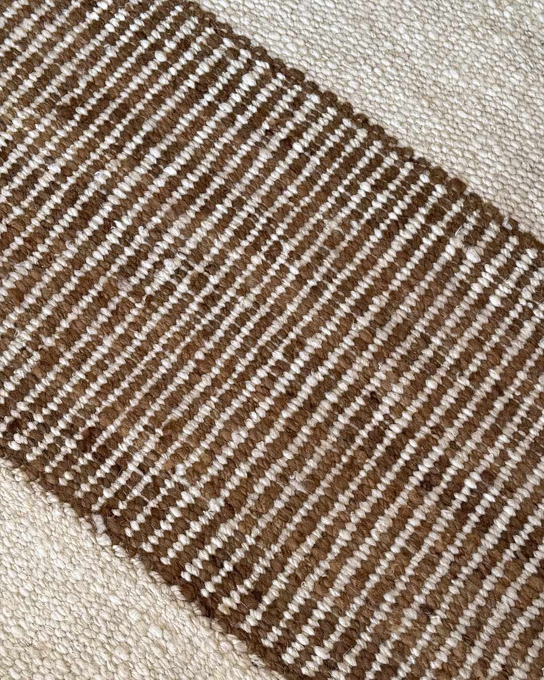 Detalle macro de alfombra Escalera en tonos natural y nuez mostrando fibras de lana