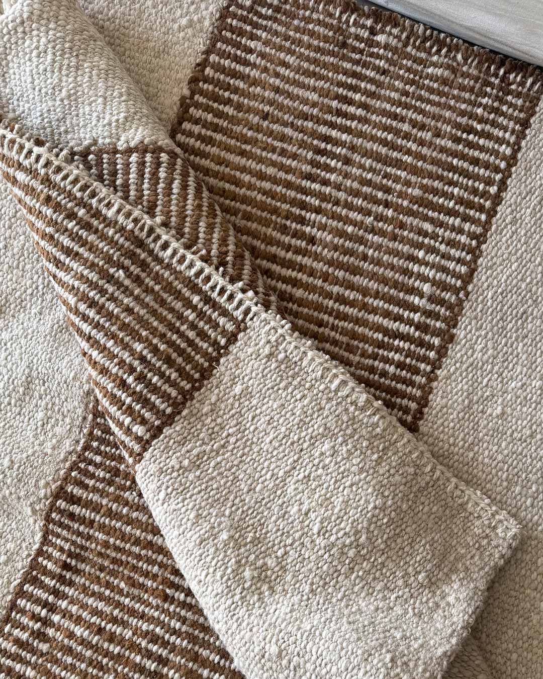 Alfombra Escalera natural y nuez en lana doblada mostrando textura y diseño lineal