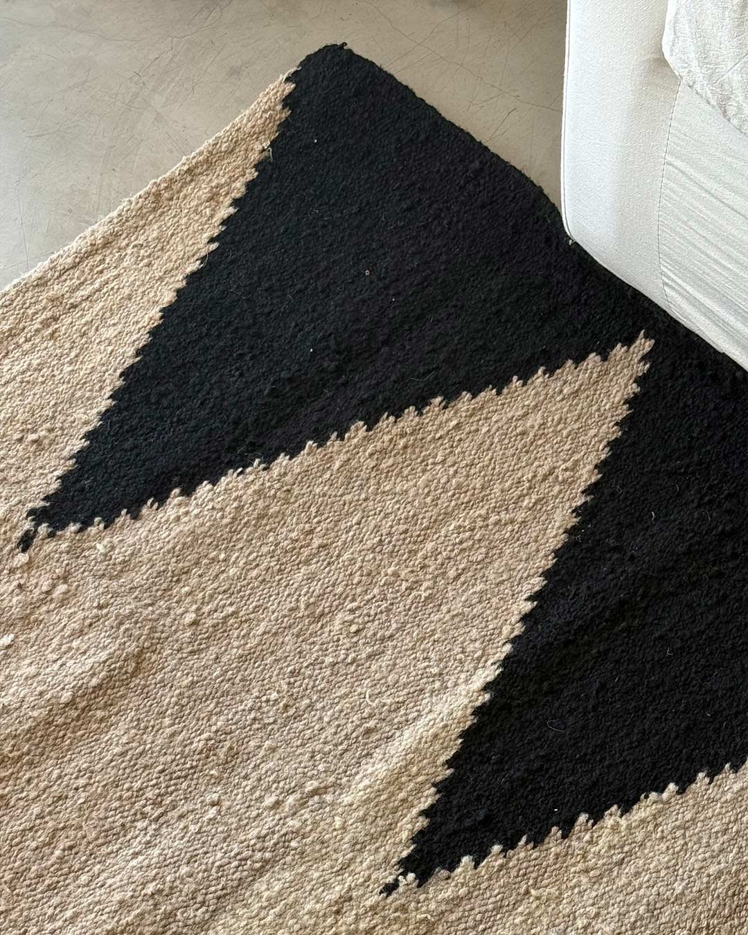 Detalle de una alfombra de lana tejida a mano con diseño geométrico en negro y arena sobre base natural.