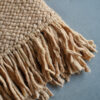 Camel-colored wool throw with handmade fringes on a concrete floor.