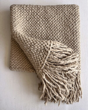 Folded beige handwoven wool throw with fringes, showcasing the texture and craftsmanship.