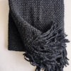 Black wool throw partially unfolded, displaying its thick texture and twisted fringes.