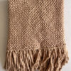 Folded wool throw in camel color with fringes, placed on a flat surface.