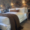 Chocolate brown wool throw draped at the foot of a bed in a bedroom with patterned wallpaper.
