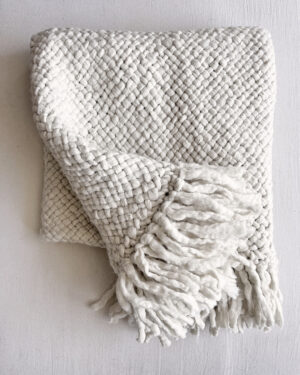 Folded natural white handwoven wool throw with fringes, showcasing a chunky weave pattern.