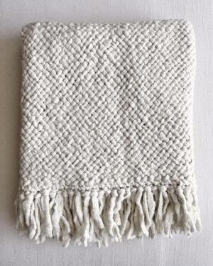 Natural white handwoven wool throw with fringes, neatly folded to show texture and weave.